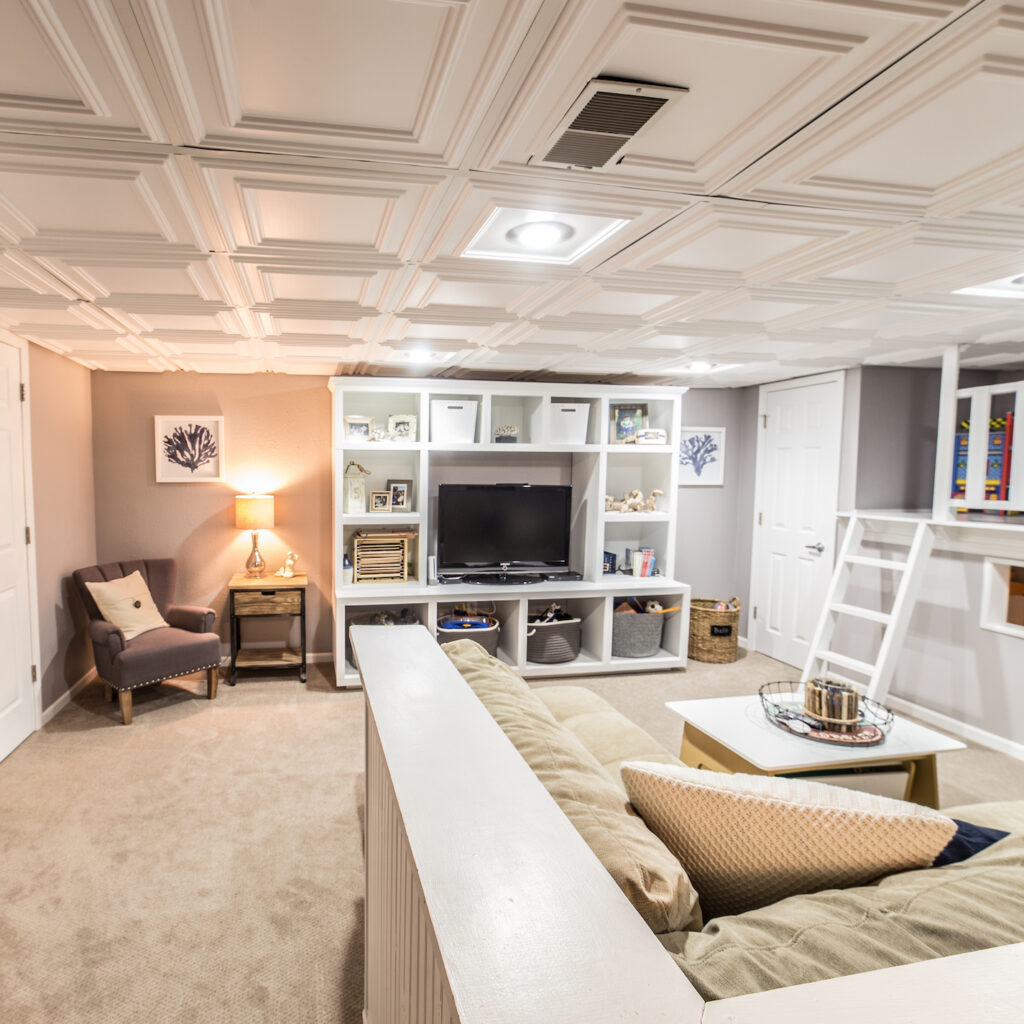 Entry way to living space in a remodeled basement with Faux tin ceilings, white entertainment center for television and cream fabric sectional couch.