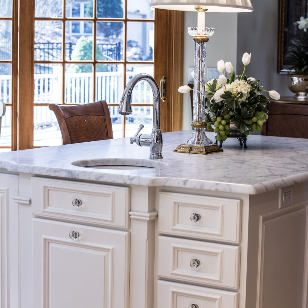 Kitchen island with Carrara marble kitchen countertop replacement, nickel plated faucet, rinse sink and white cabinets.