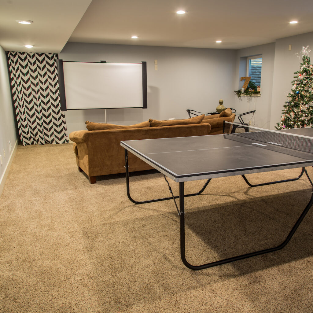 Home remodel with recessed lighting, projector screen T.V., ping pong table and brown suede couch and chaise lounge chair.